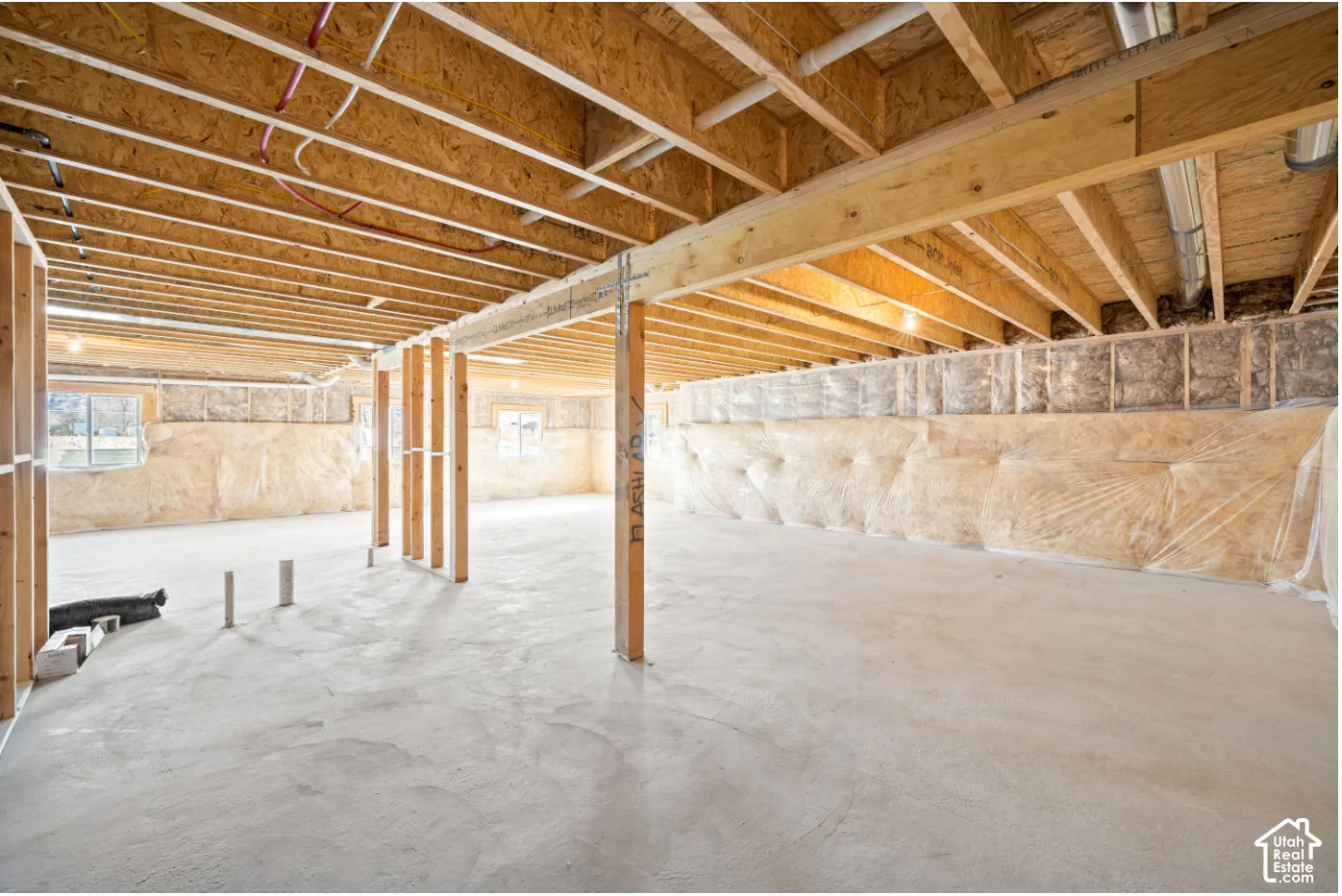 Unfinished lower level featuring concrete flooring, exposed wood joists, structural support posts, and framed window openings