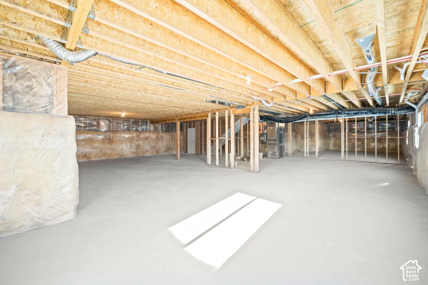 Unfinished basement featuring exposed wood joists, concrete flooring, perimeter wall framing, and visible utility runs