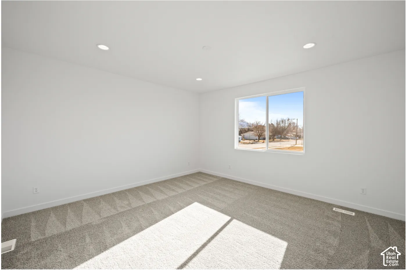 Spacious room featuring neutral carpeting, white walls, and recessed ceiling lighting