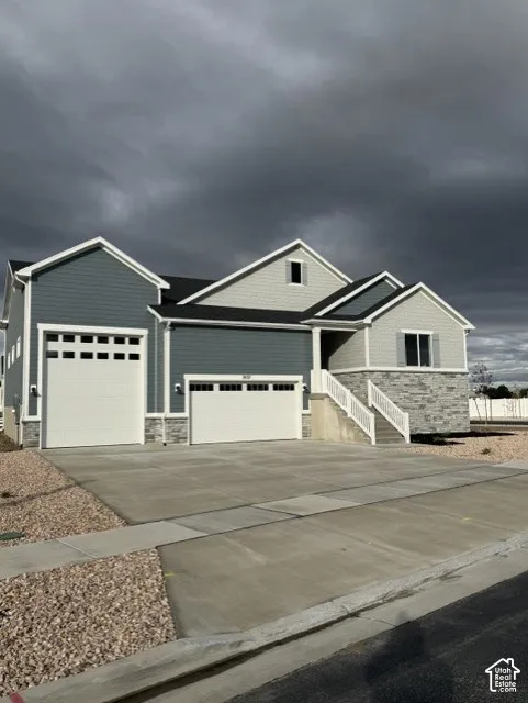 Multi-gabled exterior featuring dual-tone horizontal siding, stone veneer accents, an attached three-car garage, and a concrete driveway