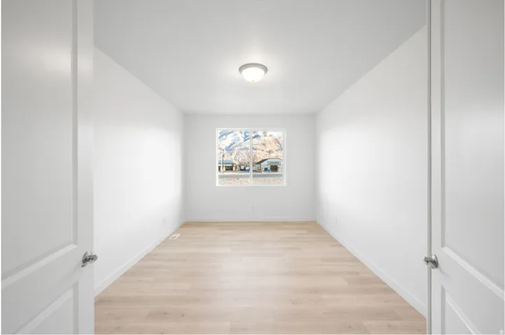 Bright interior space featuring a window with a mountain backdrop, wood-finish flooring, white walls, and a flush mount ceiling light