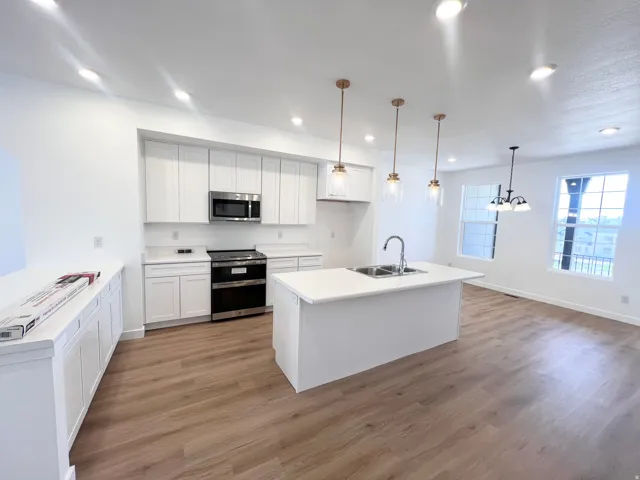 Bright kitchen featuring a central island with a double basin sink, white cabinetry with brushed gold hardware, stainless steel appliances, recessed lighting, and wood-finish flooring