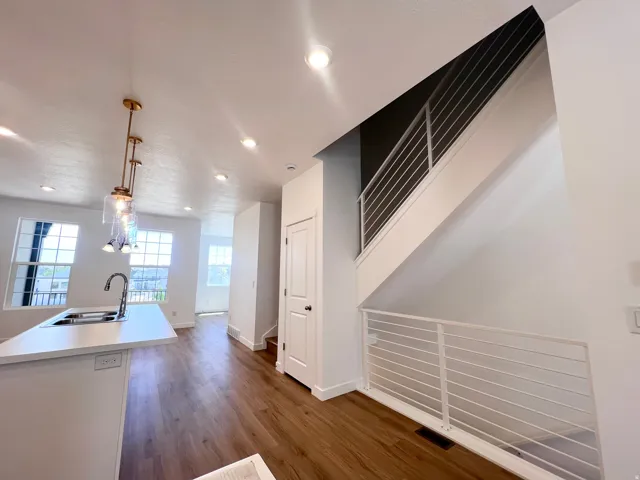 Open-concept space featuring a kitchen island with sink, wood-finish flooring, recessed lighting, a contemporary stair railing, and ample natural light from multiple windows