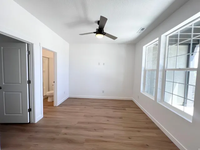 Spacious room featuring wood-finish flooring, white walls, and a ceiling fan