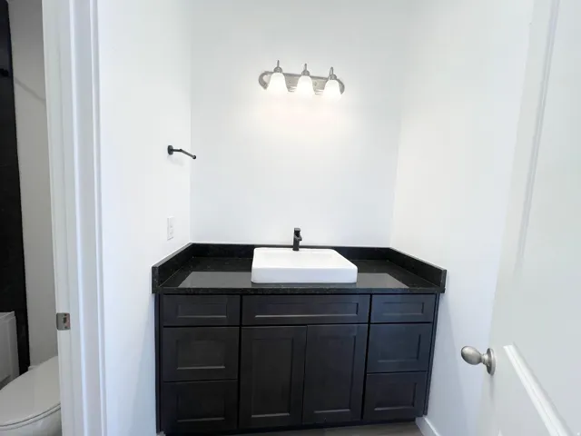 Dark wood-finish vanity with a vessel sink, dark countertop, and matte black faucet