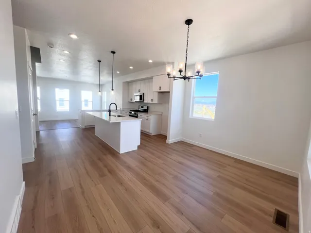 Open-concept living space with wood-finish flooring, a kitchen island with a dark faucet, white cabinetry, and recessed lighting