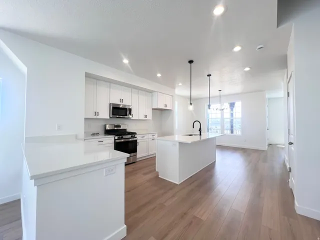 Modern kitchen featuring white cabinetry, stainless steel appliances, a center island with a black gooseneck faucet, light wood-finish flooring, and recessed lighting