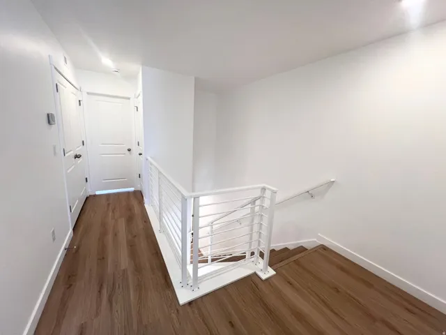 Upper-level hallway featuring wood-finish flooring, white walls, and a contemporary white metal railing system