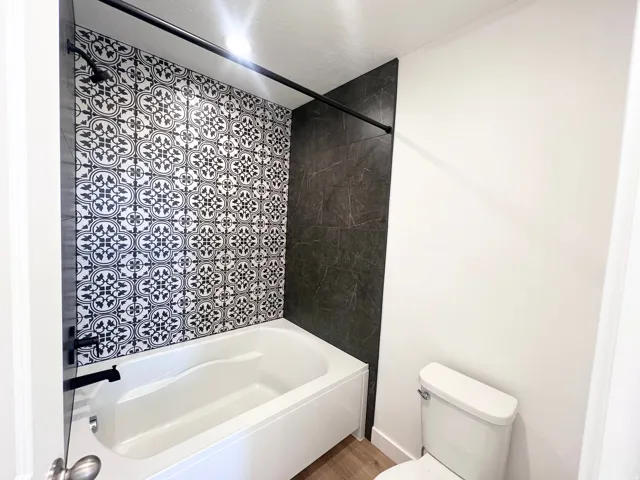 Bathroom featuring a white soaking tub, black and white patterned tile shower surround, dark large-format tile accent wall, and matte black shower fixtures
