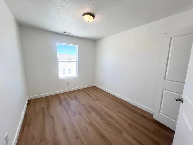 Spacious room featuring wood-finish flooring, white baseboards, and a single window