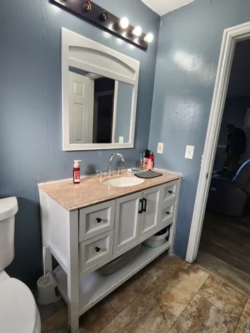 Bathroom vanity featuring a light-toned countertop with integrated sink, white cabinetry with dark hardware, and a framed mirror