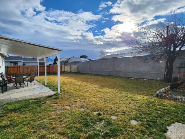 Expansive backyard featuring a covered patio with concrete flooring, a large grassy area, a concrete block privacy wall, and mature landscaping