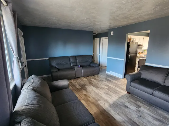 Living area featuring wood-finish flooring, two-tone painted walls with chair rail molding, and an open doorway to the kitchen