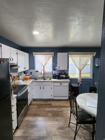 Kitchen featuring wood-finish flooring, white cabinetry, stainless steel range, and a dual-basin sink with a gooseneck faucet