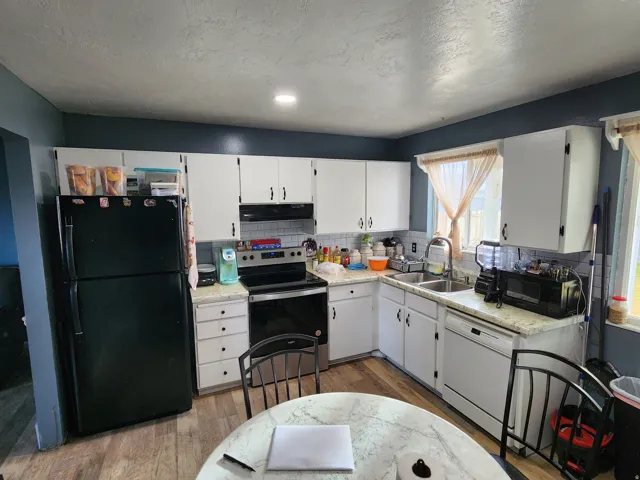 Kitchen featuring white cabinetry, subway tile backsplash, light-toned countertops, wood-finish flooring, and a stainless steel double-basin sink