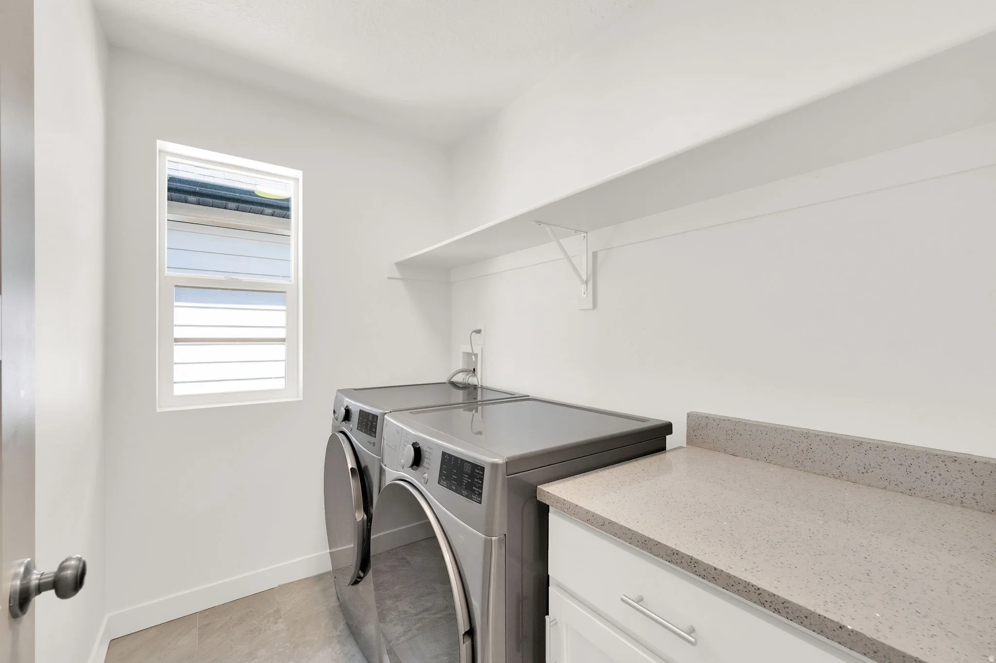 Laundry area featuring a window, built-in shelving, white cabinetry, and a light-toned countertop