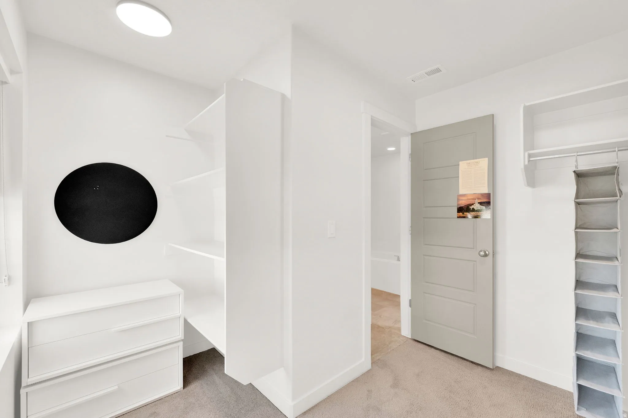 Recessed lighting illuminates a built-in shelving system, an integrated two-drawer dresser, and a gray paneled door
