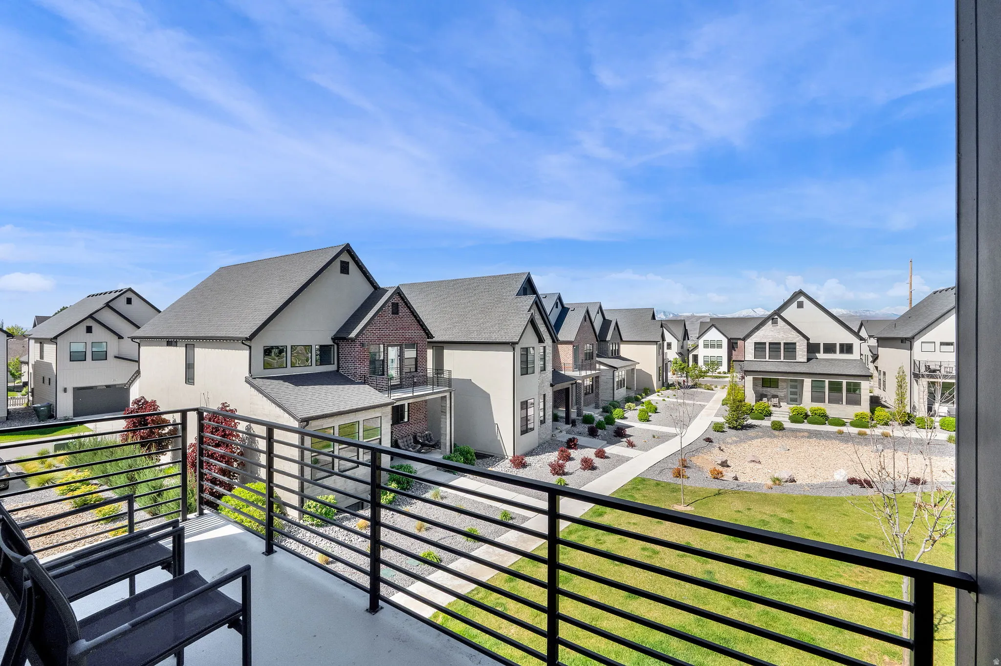 Balcony with dark metal railing overlooking a landscaped community area with green space and paved walkways