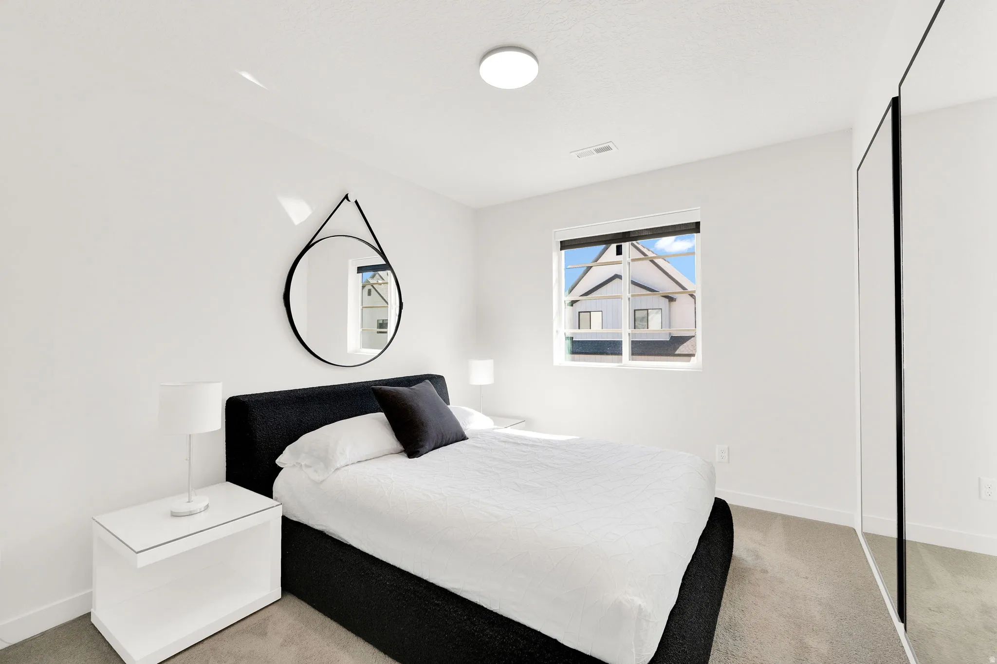 Bright bedroom featuring light-colored carpeting, white painted walls, and a window with white trim