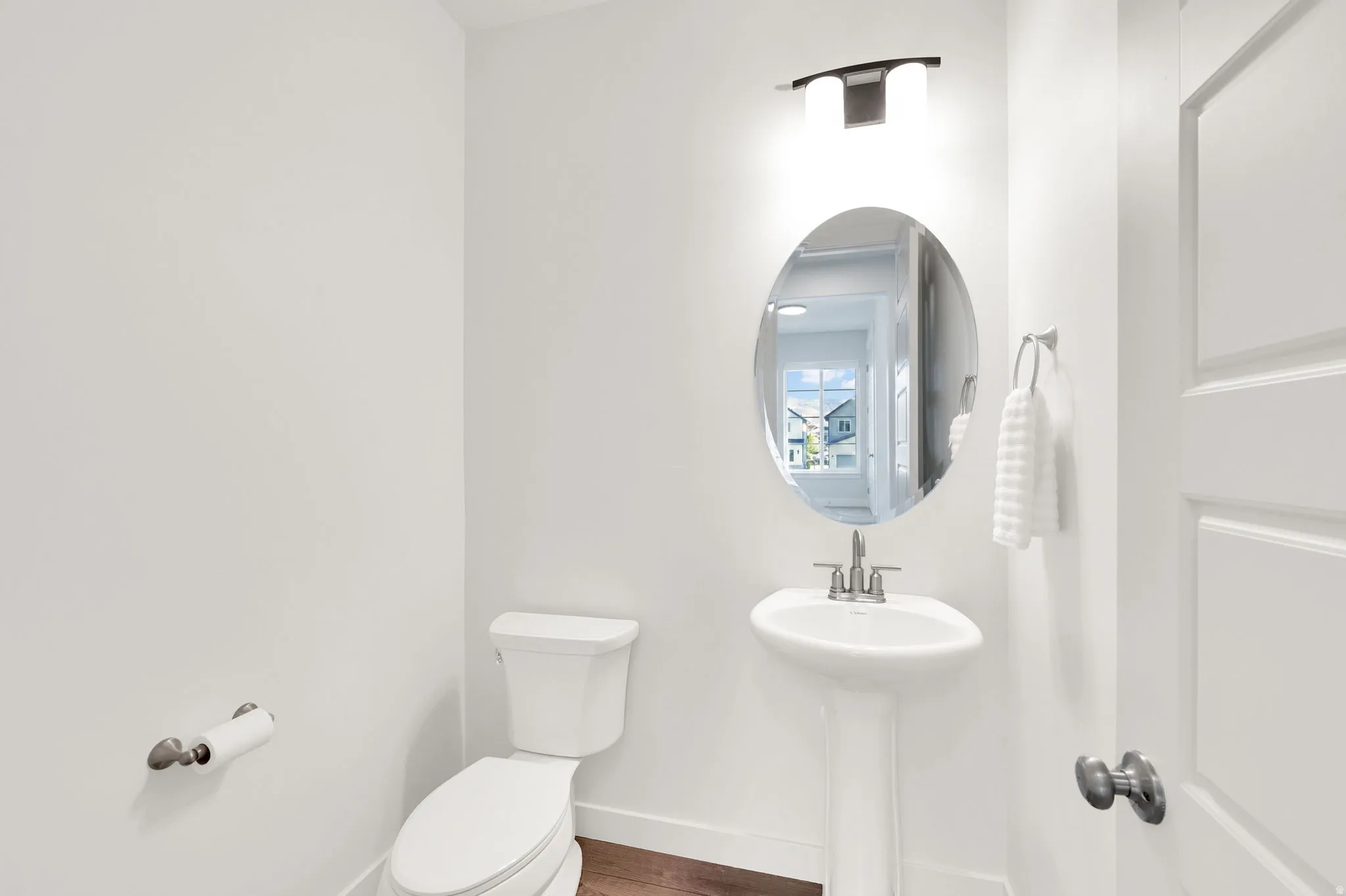 Pedestal sink with chrome fixtures, oval mirror, and contemporary vanity lighting