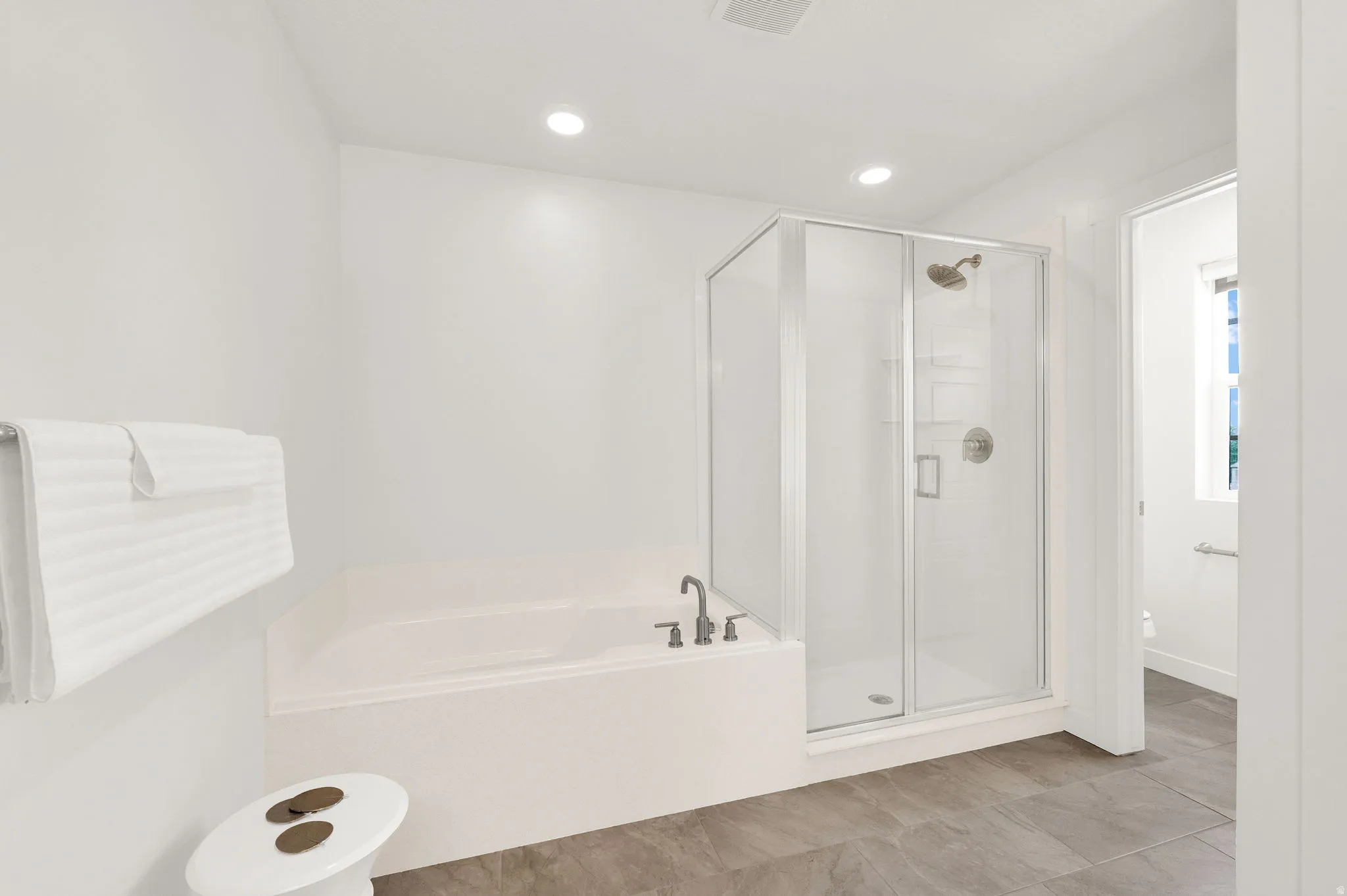 Bathroom featuring a built-in soaking tub with deck-mounted fixtures, a glass-enclosed shower with a rain showerhead, recessed lighting, and large format floor tiling