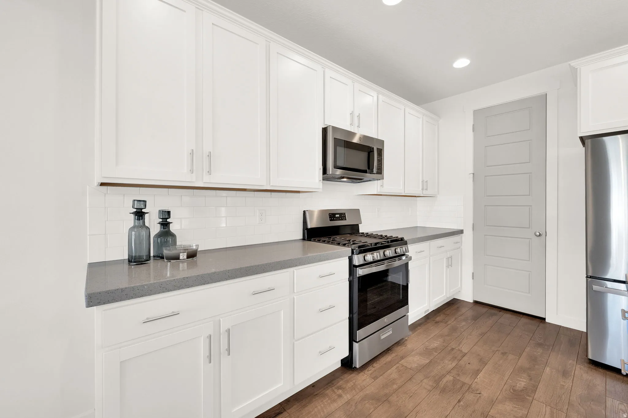 Contemporary kitchen featuring white cabinetry, stainless steel appliances, grey countertops, white subway tile backsplash, and wood-finish flooring
