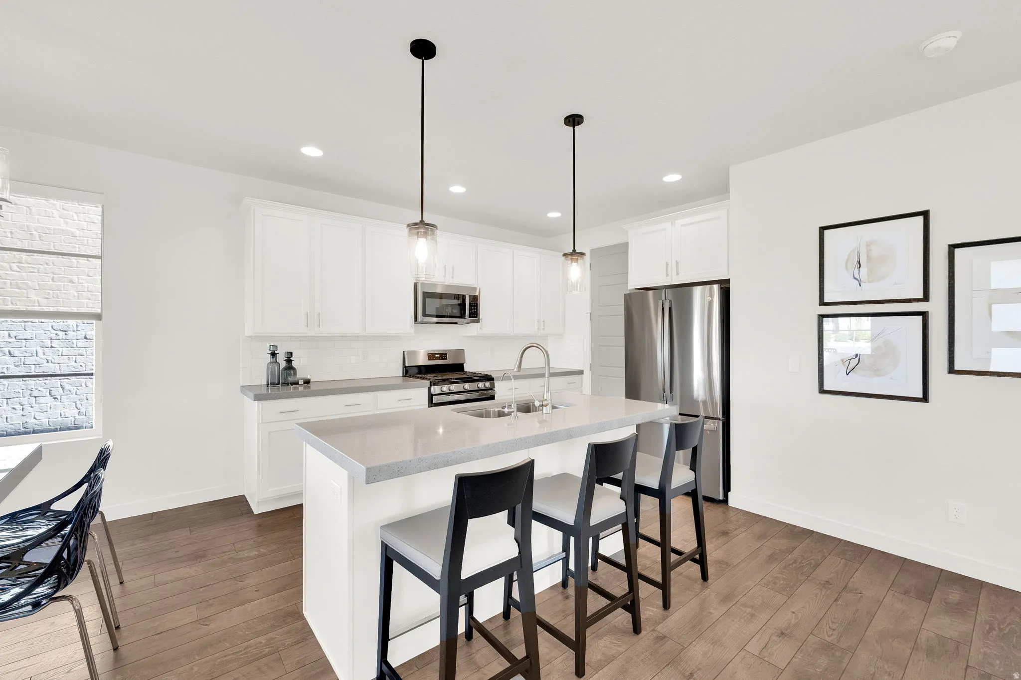 Modern kitchen featuring an expansive center island with seating, stainless steel appliances, white shaker cabinetry, pendant lighting, and wood-finish flooring