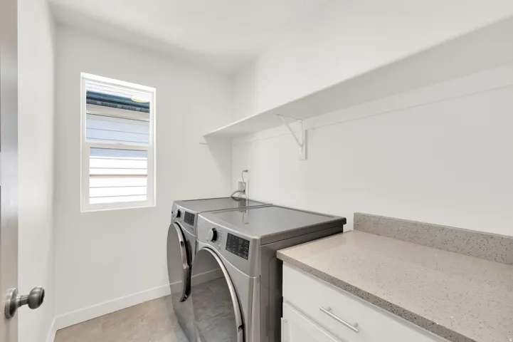 Laundry area featuring a window, built-in shelving, white cabinetry, and a light-toned countertop