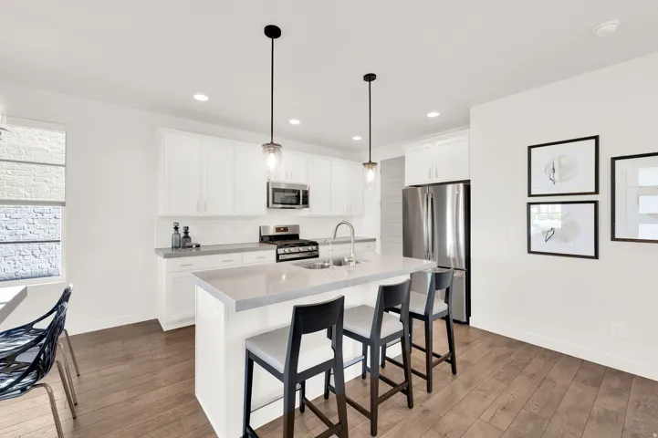 Modern kitchen featuring an expansive center island with seating, stainless steel appliances, white shaker cabinetry, pendant lighting, and wood-finish flooring