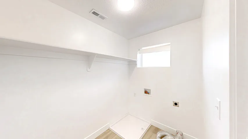 Laundry area featuring a window with blind, light wood-finish flooring, a white wall shelf, and connections for appliances