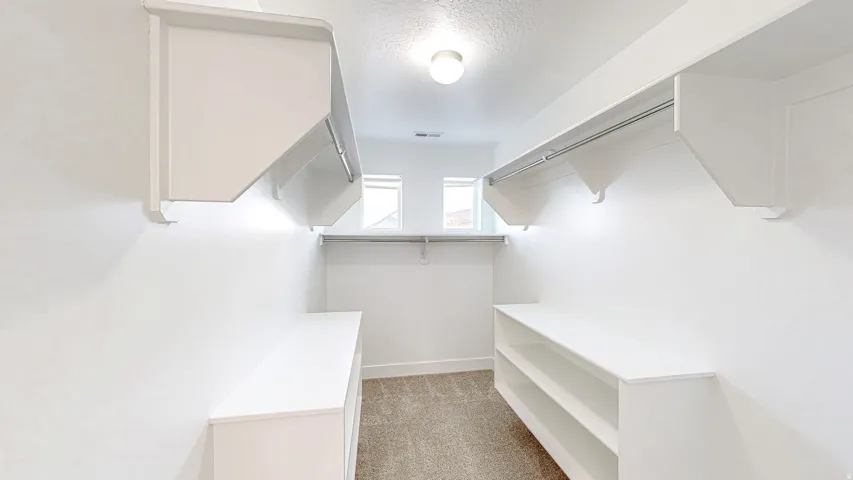 Walk-in closet featuring built-in shelving, hanging rods, two windows, and overhead lighting