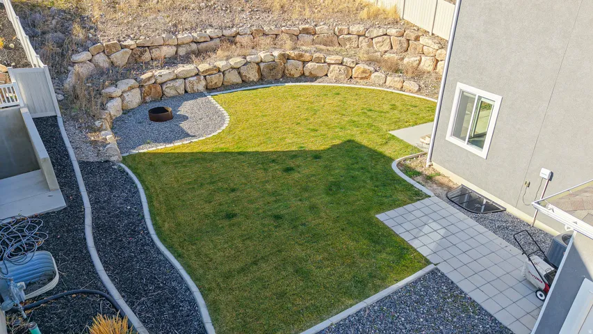 Terraced backyard featuring a manicured lawn, natural stone retaining walls, and a gravel fire pit area
