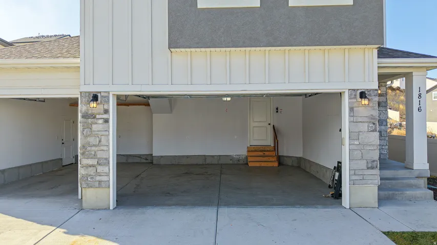 Spacious two-car garage with concrete flooring, stone veneer accents, and recessed outdoor lighting