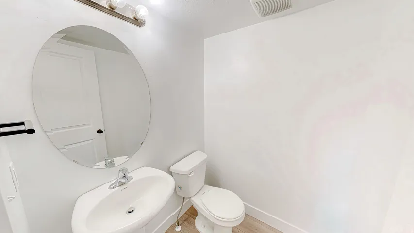 Powder room featuring a pedestal sink with chrome faucet, an oval frameless mirror, and a wall-mounted light fixture