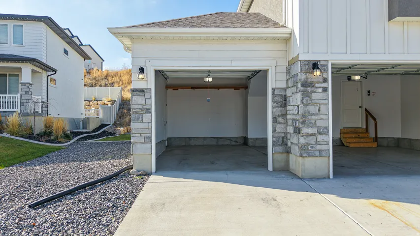 Integrated two-car garage featuring a concrete floor, overhead lighting, and interior access stairs