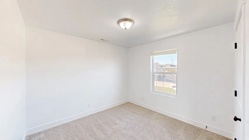 Bright interior space featuring neutral carpeting, white baseboards, and a single window with a roller shade