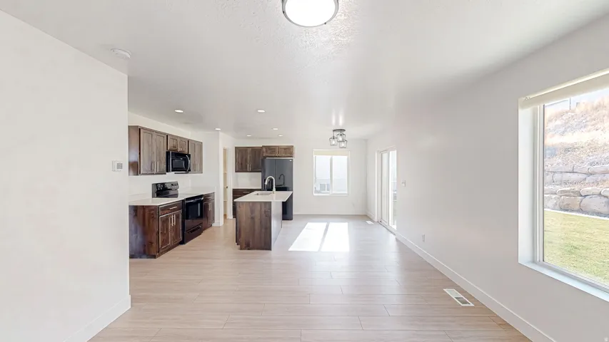 Open-concept kitchen featuring dark wood cabinetry, white countertops, and a central island with a sink