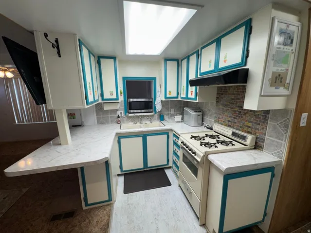 U-shaped kitchen featuring white cabinetry with teal accents, a gas range, a multi-toned tile backsplash, and a white countertop