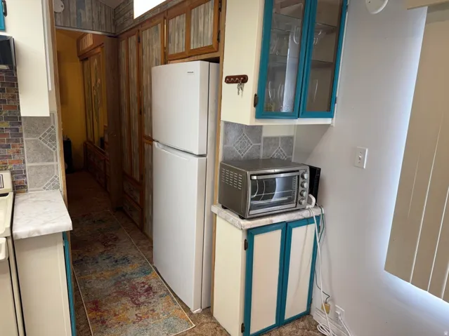 Kitchenette featuring cream cabinetry with teal trim, a white refrigerator, and glass-front upper cabinets