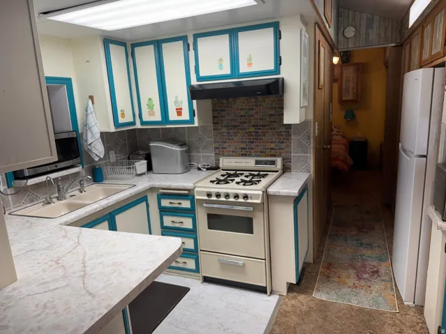 Kitchen featuring white cabinetry with teal trim, a white gas range, and a dual basin sink