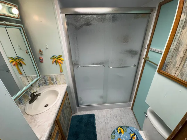 Shower with frosted glass enclosure, single vanity with integrated sink, and wood-finish cabinetry
