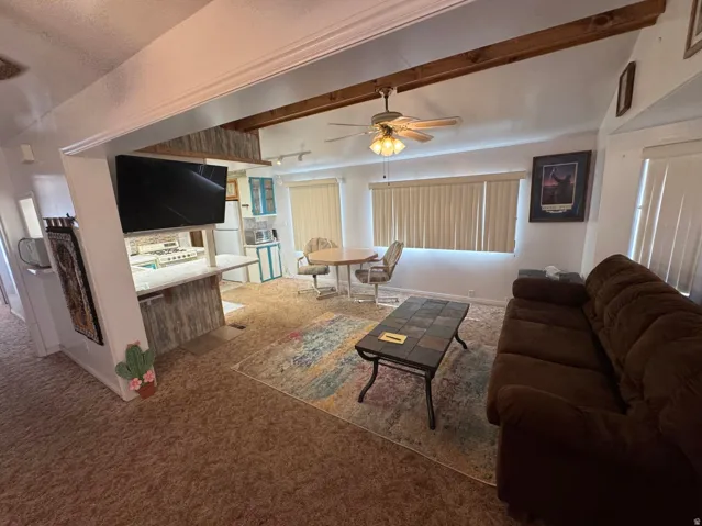 Living area featuring wood-finish ceiling beams, ceiling fan light fixture, and vertical blinds