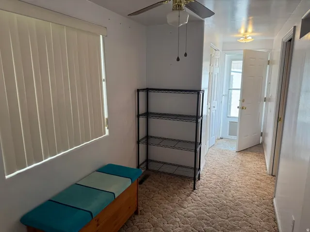 Interior space featuring light-toned vertical window blinds, a ceiling fan with integrated lighting, and textured carpeting