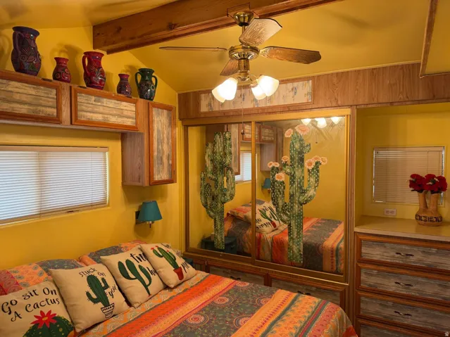 Bedroom featuring a ceiling fan with integrated lighting, wood-finish ceiling beams, built-in cabinetry with distressed wood paneling, sliding mirrored closet doors, and wood-finish wall panels