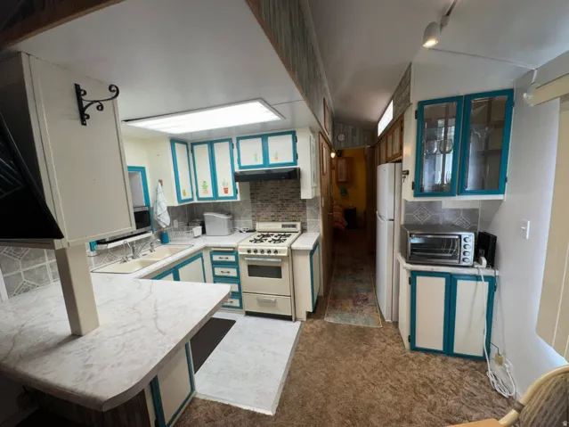Kitchen featuring U-shaped countertops, wood-finish flooring, a mosaic tile backsplash, and white cabinetry with teal accents
