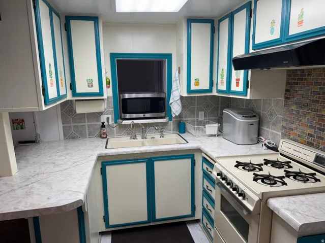 U-shaped kitchen featuring white cabinetry with turquoise trim, a built-in microwave, white countertops, a mosaic tile backsplash, and a skylight