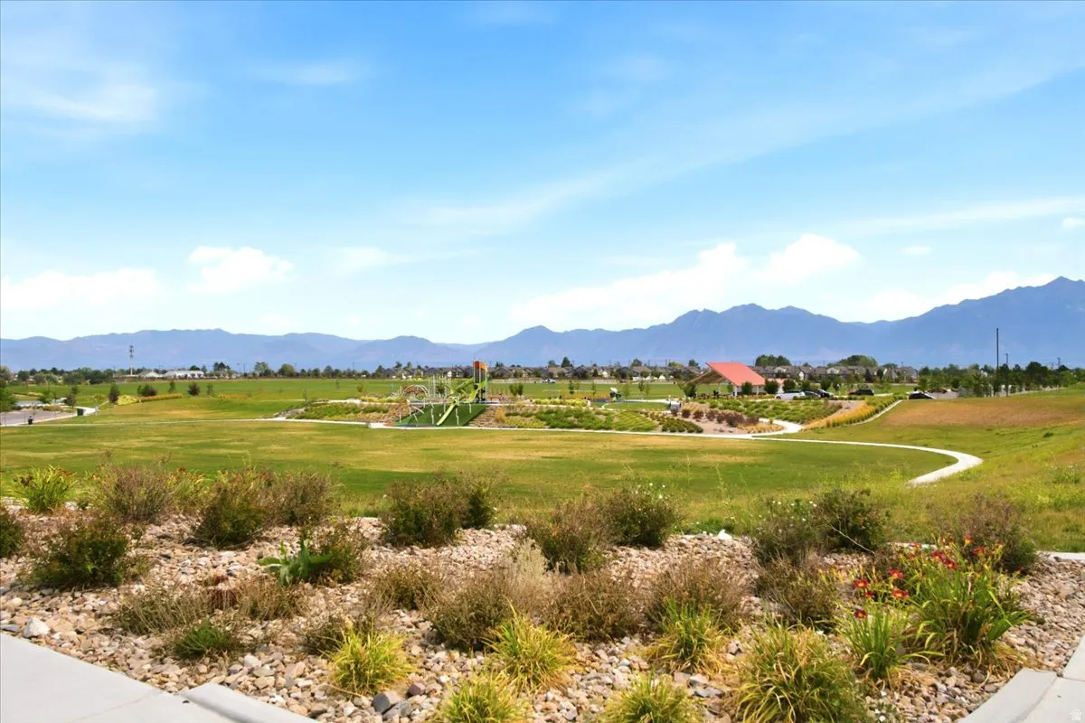 Expansive green space featuring mountain scenery, paved walking paths, and a distant playground structure