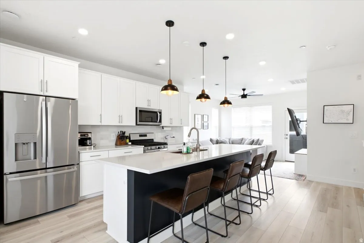 Modern kitchen featuring white cabinetry, stainless steel appliances, a center island with seating, pendant lighting, and light wood-finish flooring