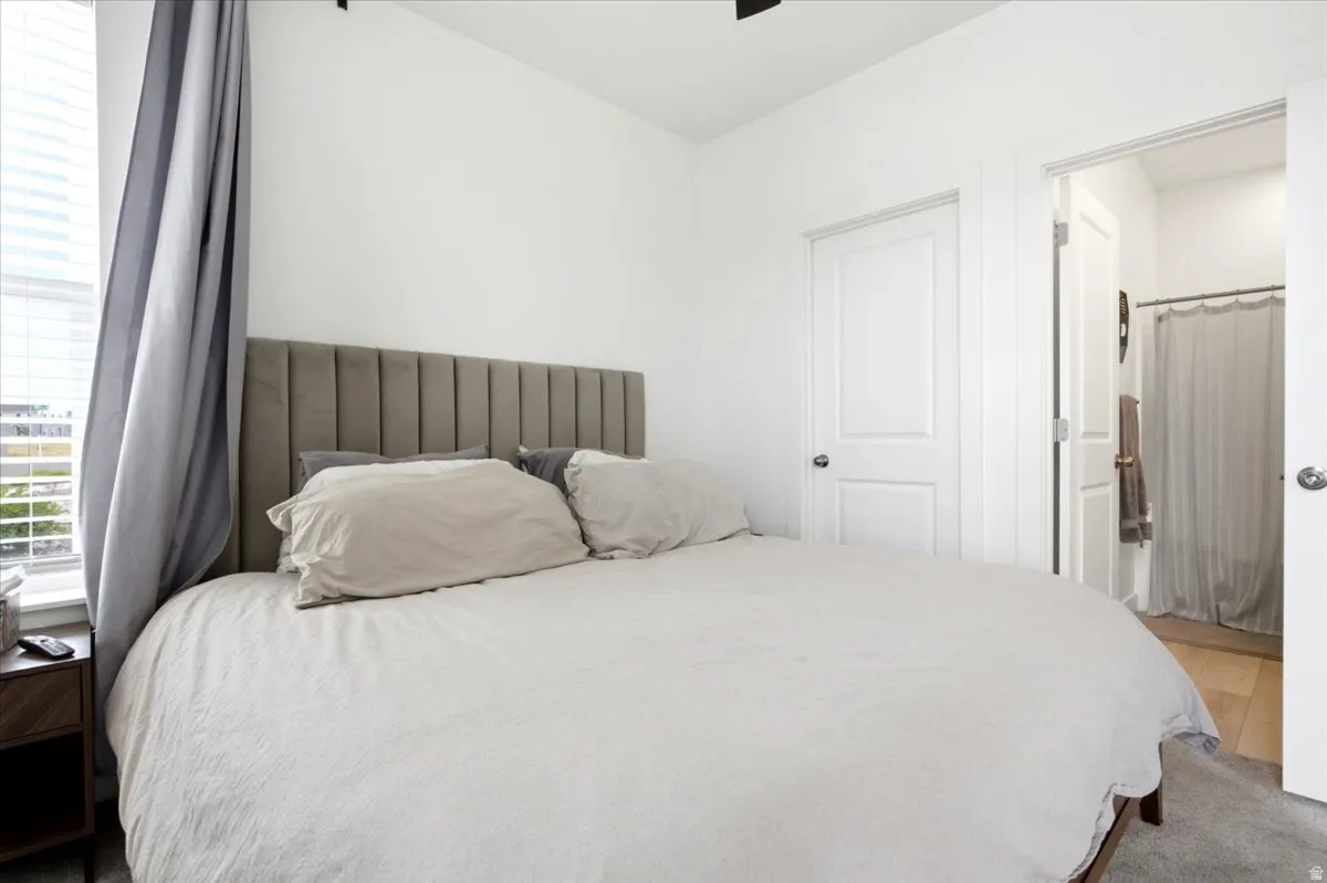 Bedroom featuring a window with blinds, a solid white door, an open doorway, and gray carpeting