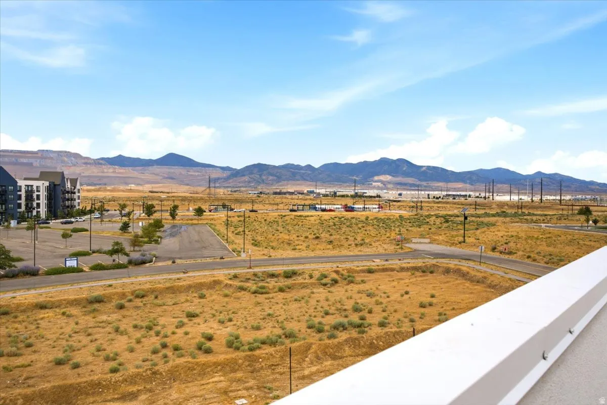 Expansive landscape with distant mountain ranges and a clear sky, featuring a modern building with balconies and a parking area